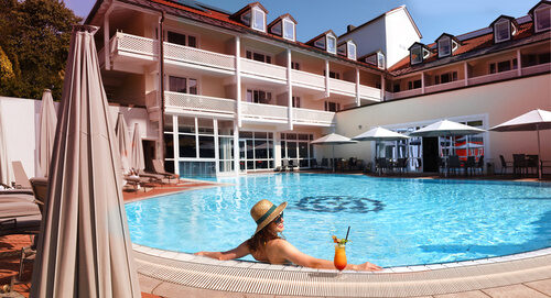 Eine Frau enstpannt im Swimmingpool im Aussenbereich des Hotels St. Wolfgang in Bad Griesbach mit einem Cocktail.