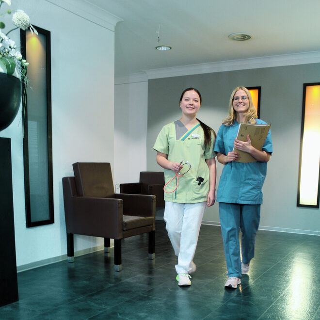 A neatly made double bed stands in a bright hotel room, illuminated by natural light from a glass door leading to a balcony.