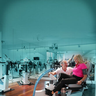 A modern gym with various exercise machines arranged neatly, lit by circular ceiling lights.