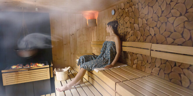 Wooden sauna benches are neatly arranged in a warm-lit room, with stacked firewood lining one wall, creating a cozy, inviting atmosphere.