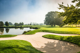 Der malerische St. Wolfgang Golfplatz Uttlau mit Sandbunker, grünem Gras und einem ruhigen Teich im Hintergrund.