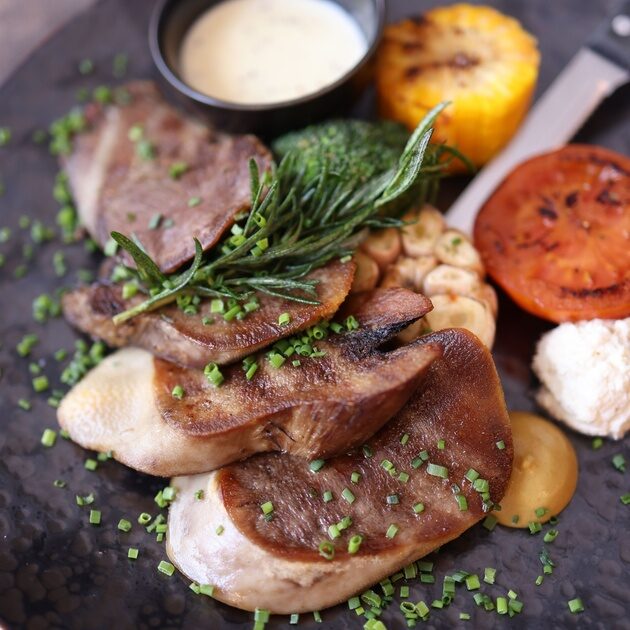 Gourmet-Fleischgericht mit gegrilltem Gemüse und Kräutern auf schwarzem Teller