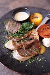 Gourmet-Fleischgericht mit gegrilltem Gemüse und Kräutern auf schwarzem Teller