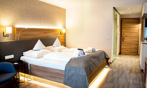 Ein Doppelbett mit weißen Kissen und Handtüchern liegt in einem modernen, gut beleuchteten Hotelzimmer. Ein Doppelbett mit weißen Kissen und Handtüchern liegt in einem modernen, gut beleuchteten Hotelzimmer. Elegantes Designparadies im Herzen des Resorts.